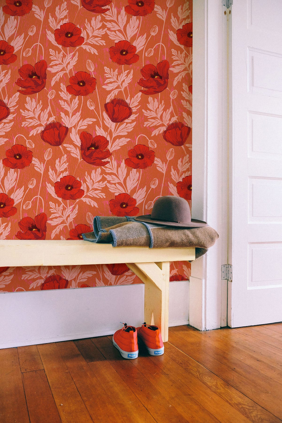 Bench with a hat and shoes against a wall with red floral wallpaper