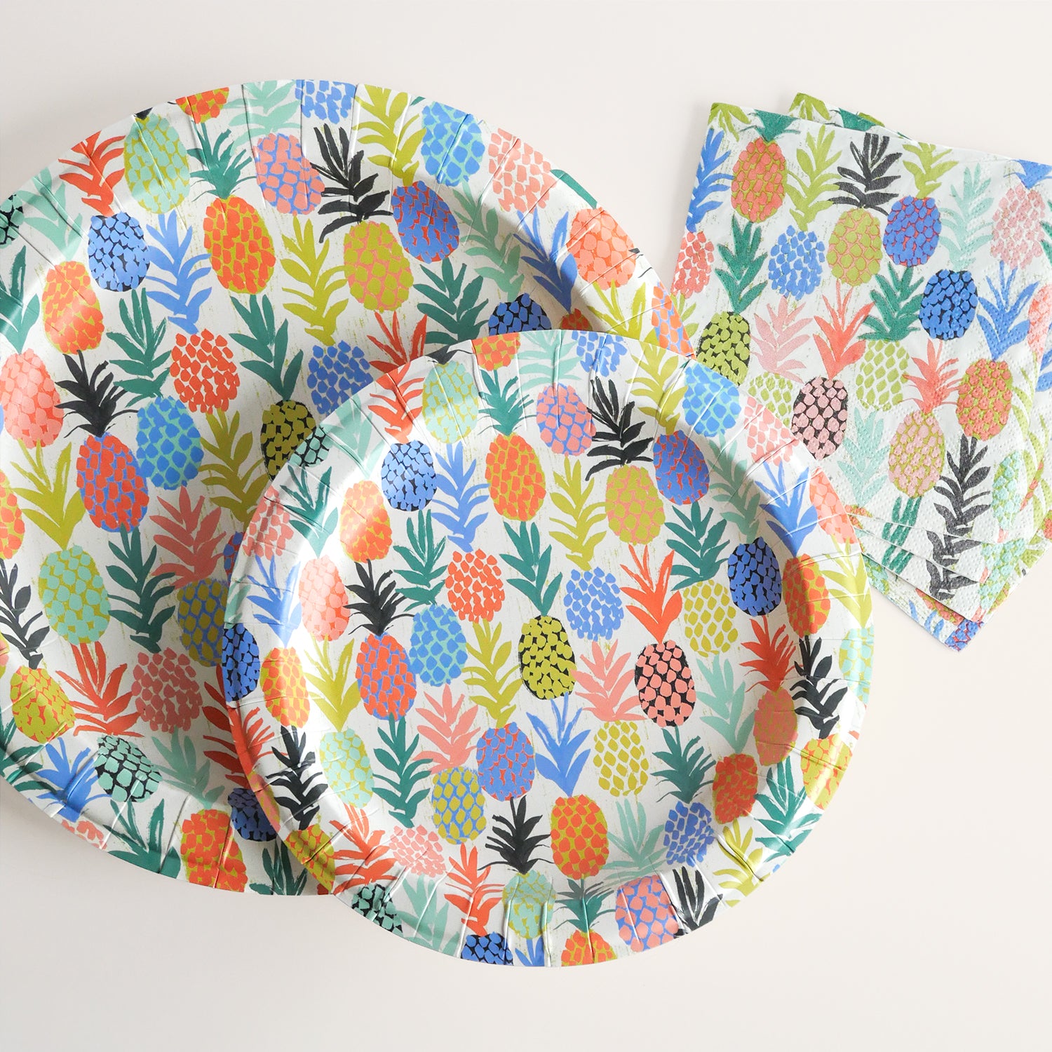 Colorful pineapple patterned paper plates and napkins on a white background
